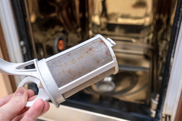 Maintenance and repair of dishwashing mashine, hand holding a dirty drain filter