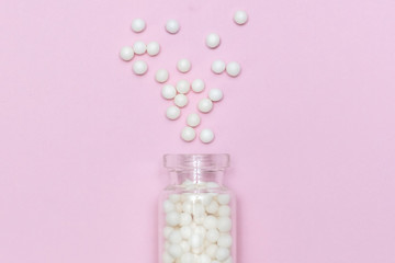 Homeopathic globules scattered from a clear glass bottle on light pink background, alternative homeopathy medicine concept
