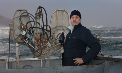 A captain of a fish trawler with binoculars in stormy weather on the Atlanik. Cable winches for nets are next to the man. Strong waves with spray can be seen in the background.