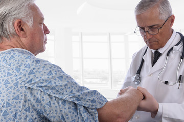Obraz premium Closeup of a elderly male patient wearing a hospital gown as a doctor examines his right arm. Focus is on the patient.