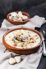 Clam chowder in a brown plate. The main ingredients are shellfish, broth, butter, potatoes and onions.