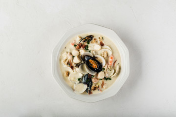 Clam chowder in a white plate. The main ingredients are shellfish, broth, butter, potatoes and onions.