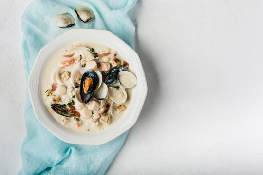 Clam chowder in a white plate. The main ingredients are shellfish, broth, butter, potatoes and onions.