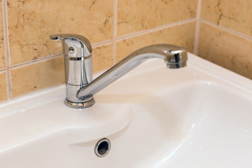 Chrome crane on the ceramic wash basin in the bathroom close up.
