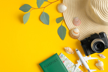 Summer travel accessories on yellow background. Flat lay beach hat, vintage camera, plane, map, passport, seashells and green leaves. Holiday trip planning concept