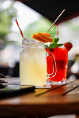 Ein gelber und ein Roter Cocktail in einer Bar auf einem Holztisch mit früchten angerichtet