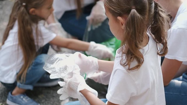 A girl is collecting the garbage. She is picking up the rubbish with group of people. Children are cleaning the forest.