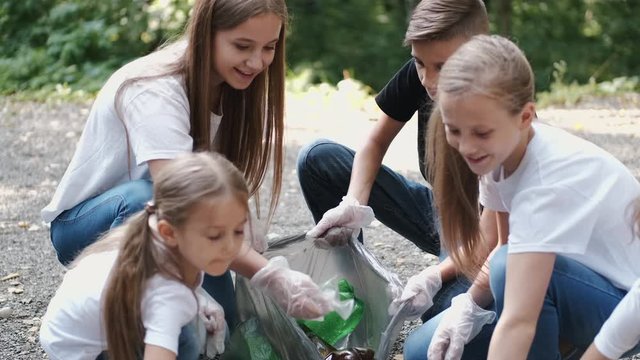 People collect the plastic. Young volunteer with group of kids pick up the garbage. Children are in the forest.