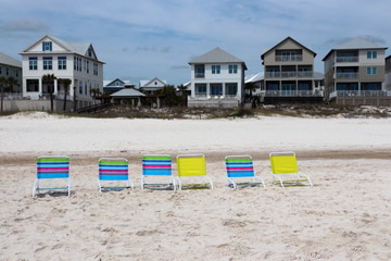 Cloudy seascape with colorful beach chairs on a white sand in a freshly built after hurricane houses for vacation rentals in a shallow depth of field. Alabama Gulf Shores beach area, USA.