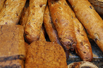 Close up view, heap and stack of OLIVENSTANGE, olive French Baguettes, and various type of rustic and crusty wheat breads at display of bakery store. 