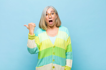 senior or middle age pretty woman looking astonished in disbelief, pointing at object on the side...