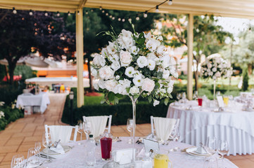 Round table set for meal. White tablecloth, empty plates, forks and knives. Fresh flowers of roses, as a decoration of a wedding table.