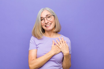 senior or middle age pretty woman feeling romantic, happy and in love, smiling cheerfully and holding hands close to heart