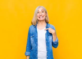 senior or middle age pretty woman looking happy, proud and surprised, cheerfully pointing to self,...