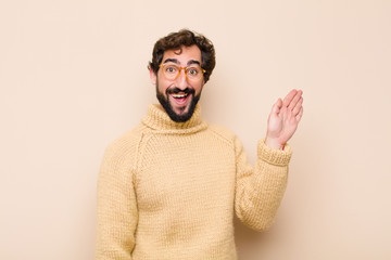 young cool man smiling happily and cheerfully, waving hand, welcoming and greeting you, or saying...
