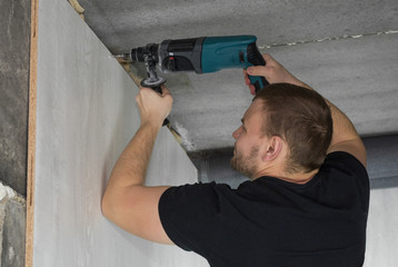 Builder worker with electric hammer drill making hole in wall in apartment