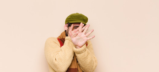 young cool bearded man covering face with hand and putting other hand up front to stop camera,...