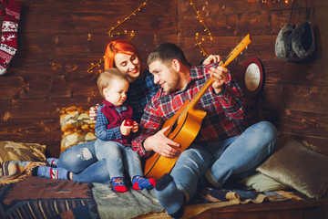 Family sitting at home. Father playing on a guitar.