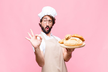 young crazy baker man holding bread against pink wall