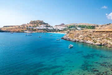 Fototapeta na wymiar Boats anchored on sea near village of Lindos, Acropolis of Lindos in background (Rhodes, Greece)