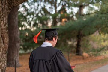 Young graduate in cap and gown walking across university campus