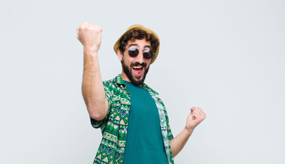 young tourist man shouting triumphantly, looking like excited, happy and surprised winner, celebrating against white wall