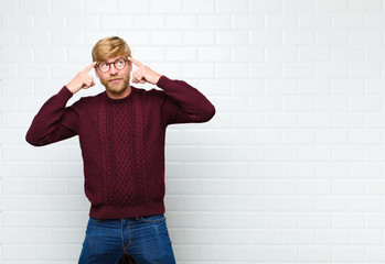 young blonde man feeling confused or doubting, concentrating on an idea, thinking hard, looking to copy space on side agaist vintage tiles wall