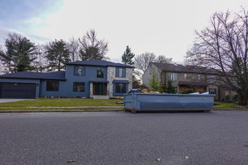 Large home on a residential street with a long blue dumpster on the road in front