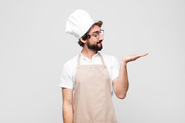 young crazy chef feeling happy and smiling casually, looking to an object or concept held on the...