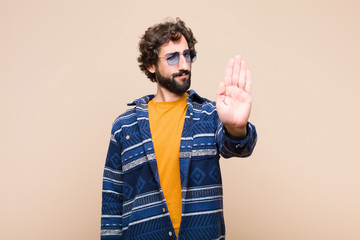 young crazy cool man looking serious, stern, displeased and angry showing open palm making stop...