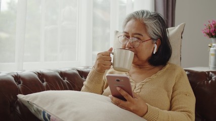 Senior woman use wireless earphone listening music and drink coffee