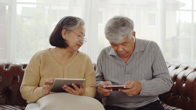 Joyful Senior couple using technology device at home - Powered by Adobe
