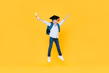Fototapeta na wymiar Schoolboy with graduate cap smiling and jumping on yellow background