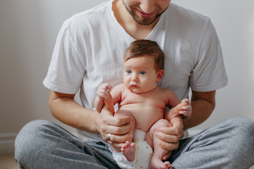 Happy Caucasian father holding newborn baby on laps knees. Man parent embracing rocking child...
