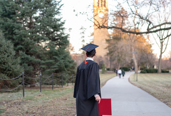 Young graduate in cap and gown walking across university campus