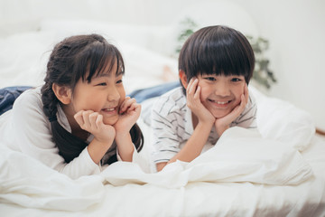 Portrait of happy Asian boy and girl playing in white bedroom, brother and sister put their smile face on hand, family concept for kid insurance