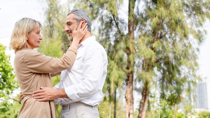 Happy romantic Caucasian couple in love at park, wife hand touching husband face and he wrapping around her, they gaze into eyes, retirement insurance banner for Valentine or anniversary concept