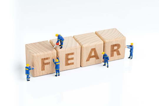 Cube wooden block with alphabets combine the word FEAR with miniature people men help building on white background using as greed and fear in investment, financial risk or afriad of crisis
