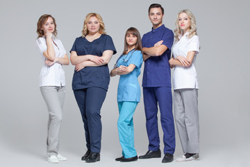 Successful team of medical doctors are looking at camera while standing on grey background