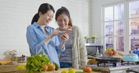 female friends chef cooking together concept. group of asian women roommates making breakfast while checking mobile phone and laughing cheerful. healthy lifestyle friendship prepare meal home kitchen