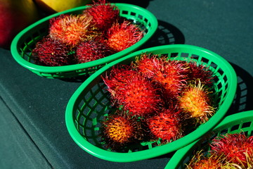 Green baskets of spiky red rambutan fruit at a market
