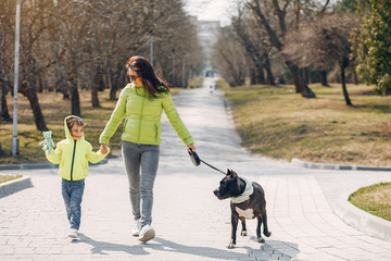 Beautiful mother with daughter. Family in a spring park. Woman in a green jacket. Family with a big dog