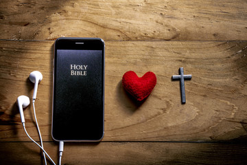 Bible app in smart phones with red heart and silver cross on wooden table, read and listen to the...