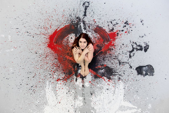 Young naked woman sitting on an artistic colour stain in the studio, copy space