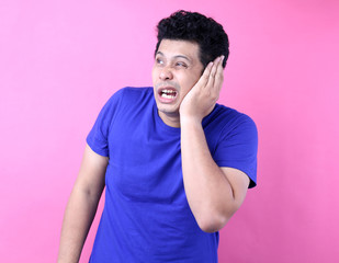 Portrait of Asian male having ear pain touching his painful head isolated on pink a background in studio.