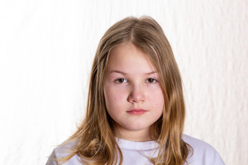 Portrait of blond beautiful girl 10 years old in front on light background, looking at camera,...
