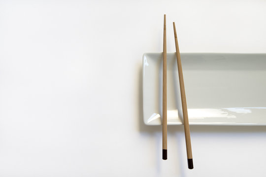  Wooden pairs of chopsticks and ceramic dish on white background. rectangular plate isolated. top view. 