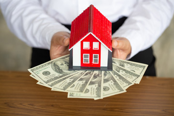 Businessmen and investors in the purchase of a home purchase contract with a broker or real estate agent are satisfied with the contract.Businessmen holding a red roof house on banknotes.