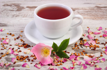 Cup of tea with wild rose flower on old rustic wooden background