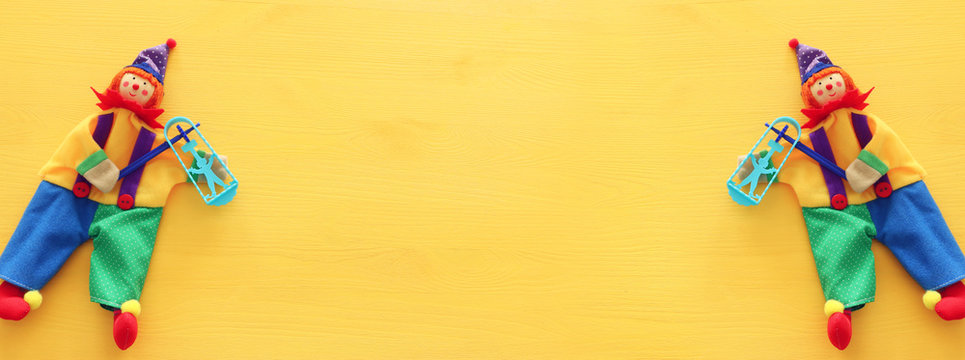 Party colorful noisemaker and cute clown over yellow wooden background . Top view, flat lay